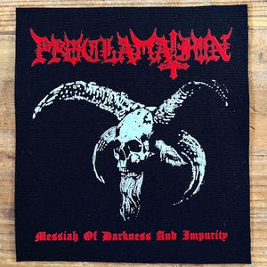 Peut inclure: Écusson carré noir avec le mot "PROCLAMATION" en rouge gothique au-dessus d'un crâne blanc et turquoise avec des cornes. Le texte "Messiah Of Darkness And Impurity" est imprimé en rouge en bas.