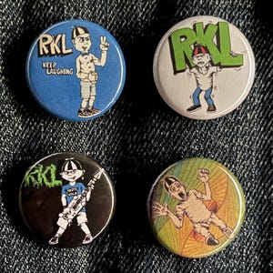 May include: Four round buttons with cartoon illustrations. One button is blue with the text "RKL" and "KEEP LAUGHING". Another is white with green "RKL" text. A third is black with a guitar-playing figure. The last is a colorful button with a figure.