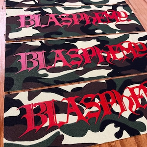 May include: Four rectangular fabric patches featuring a camouflage pattern in shades of green, brown, and cream. Each patch displays the word BLASPHEME printed in a stylized, jagged red font that transitions from a lighter pink to a deep red.