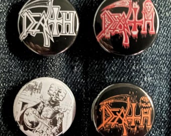 May include: Four round metal pinback buttons with black backgrounds. Two buttons feature the word "DEATH" in white and orange, respectively. One button has a red design, and another has a black and white illustration.
