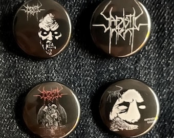 May include: Four black metal button pins with white and red graphics. The pins feature various designs, including a skull-like face, band logos, and a skeletal figure. The pins are round and have a shiny finish.