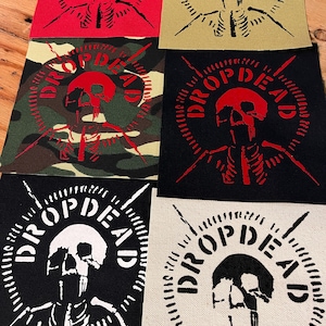 Puede incluir: Seis parches de tela cuadrados con un gráfico de un cráneo y una caja torácica rodeados por el texto DROP DEAD. Los parches vienen en varios colores, incluyendo rojo, beige, camuflaje, negro con tinta roja, negro con tinta blanca y blanco hueso.