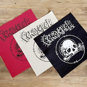 May include: Three square patches in red, off-white, and black, each with the word "CONQUEROR" in a spiky font. A skull and crossbones design is visible on each patch. The patches are arranged on a wooden surface.