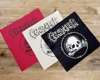 May include: Three square patches in red, off-white, and black, each with the word "CONQUEROR" in a spiky font. A skull and crossbones design is visible on each patch. The patches are arranged on a wooden surface.