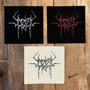 May include: Three square patches with the text "Sadistic Intent" in a gothic font. One patch is black with white text, another is black with red text, and the third is off-white with black text. The patches are on a wooden surface.