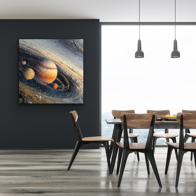 May include: A square canvas art piece depicting a vibrant, abstract representation of a planet with rings and smaller celestial bodies. The artwork features shades of orange, brown, and blue, creating a cosmic scene. The painting is displayed on a dark gray wall.