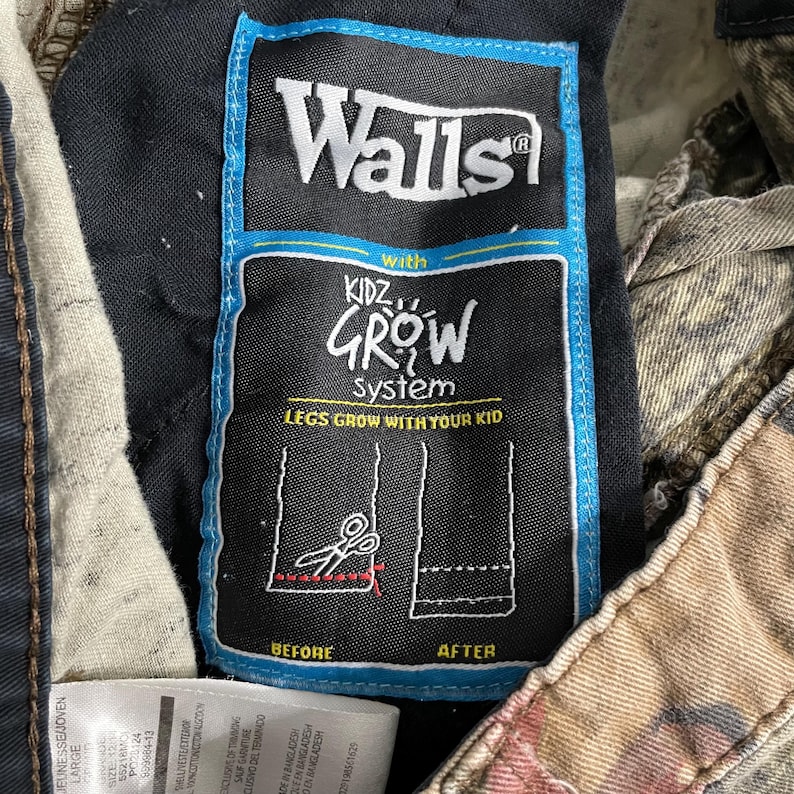 May include: Close-up of a tag on a pair of camouflage pants. The tag reads "Walls" and "Kidz Grow System: Legs Grow With Your Kid." The tag has a blue border and shows a diagram of how to lengthen the pants.