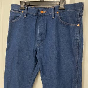 May include: Dark blue denim jeans with copper-colored rivets and button closures. The jeans are hanging on a black hanger. The jeans have a classic five-pocket design.