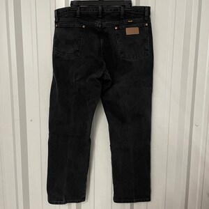 May include: Black denim jeans with a classic five-pocket design. The jeans have a straight leg fit and a brown leather patch on the back. The jeans are hanging on a black hanger.