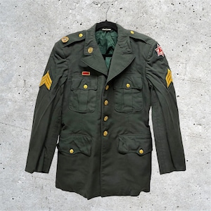 May include: An olive green military service jacket featuring gold-tone buttons, four front pockets, and yellow chevron rank insignia on both sleeves. A red and white star patch is on the left shoulder, with a small red rectangular bar on the chest.