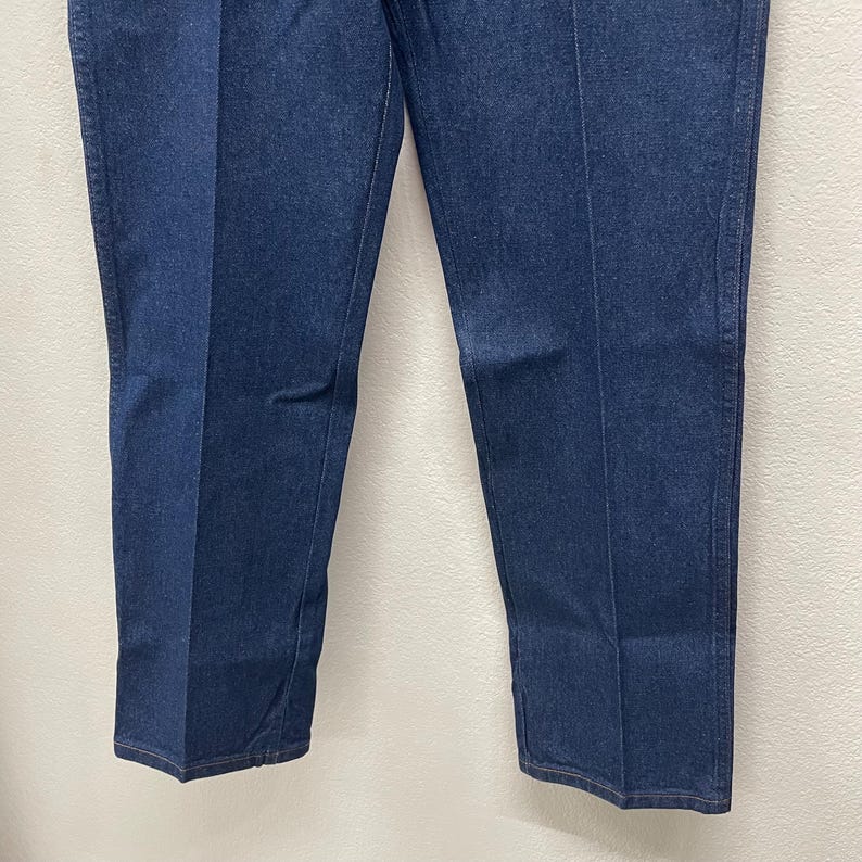 May include: A pair of dark blue denim jeans. The jeans have a classic five-pocket design, a straight leg, and a button and zipper closure. The denim fabric appears to be a medium weight.