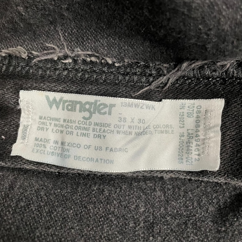 May include: Close-up of a black Wrangler jeans label. The label includes the brand name, size 38 x 30, and care instructions. Made of 100% cotton in Mexico.