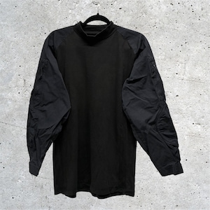 May include: A black long-sleeve shirt featuring a mock neck collar and raglan sleeves. The sleeves are constructed from a different fabric texture than the main body and include zippered utility pockets on the upper arms and reinforced elbow patches.