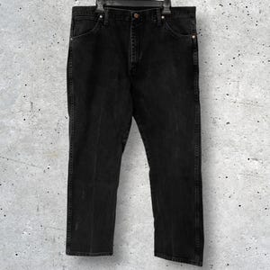 May include: Black denim jeans hanging on a black hanger. The jeans have a classic five-pocket design with a straight leg fit. The denim appears to be slightly faded, giving them a worn look. The jeans are a dark, solid black color.