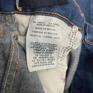 May include: Close-up of a blue denim garment's interior, showcasing a white tag with text in English, Spanish, and French. The tag includes details like "MADE IN MEXICO" and various product codes. The fabric is a classic denim weave.