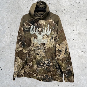 May include: A long-sleeve hooded sweatshirt featuring a camouflage pattern in shades of brown, green, and black. The center of the chest displays a white embroidered graphic of a deer skull with antlers above the text REDHEAD in white lettering.