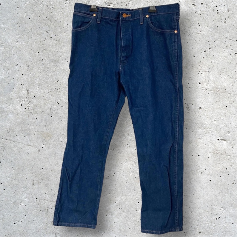 May include: Dark blue denim jeans with a classic five-pocket design. The jeans have a button and zipper closure, and copper-colored rivets. The straight-leg style is visible in this full-length shot.