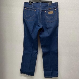 Op de afbeelding: Donkerblauwe denim jeans met het Wrangler-logo op de achterzakken en een leren patch. De jeans hebben een klassiek vijf-zakken ontwerp en een rechte pijp. De stiksels zijn in een contrasterende bruine kleur.