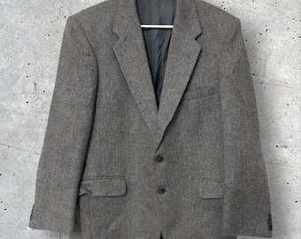 May include: A gray herringbone blazer with a two-button closure, notched lapels, and two front pockets. The blazer is hanging on a white hanger against a textured gray background. The brand name "PARK" is visible on the label.