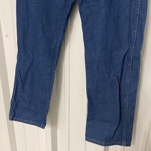 May include: Close-up of blue denim jeans. The jeans have a classic straight leg cut and are made of a medium-wash denim fabric. The image shows the lower portion of the jeans, highlighting the leg and hem details.