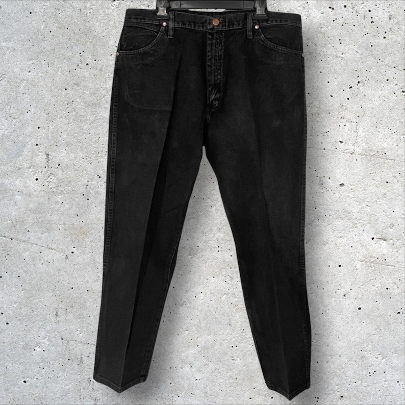 May include: Black denim jeans hanging on a hanger. The jeans have a classic five-pocket design, a button and zipper closure, and a straight leg. The denim appears to be a dark wash, with subtle fading. The jeans are a versatile wardrobe staple.