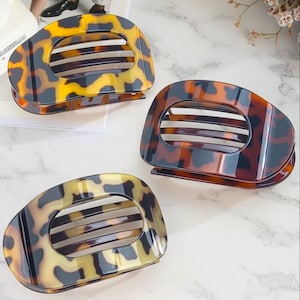 May include: Three tortoise shell hair clips with an oval shape and a slotted design. The clips have a marbled pattern in shades of brown, yellow, and black. These accessories are ideal for securing hair.