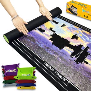 Op de afbeelding: Een zwarte vilten puzzelmat met een gedeeltelijk geassembleerde puzzel van 1000 stukjes met een stadsgezicht. De mat meet 75 x 50 cm. Een doos van de puzzel staat op de achtergrond, samen met een stapel kleurrijke puzzelsorteerbakken.