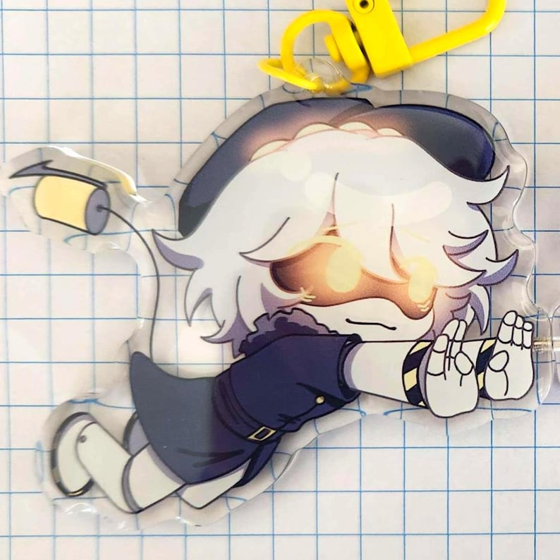 May include: A clear acrylic charm featuring a cartoon character with white hair, a dark blue outfit, and glowing yellow eyes. The charm has a yellow clasp and is on a grid background.