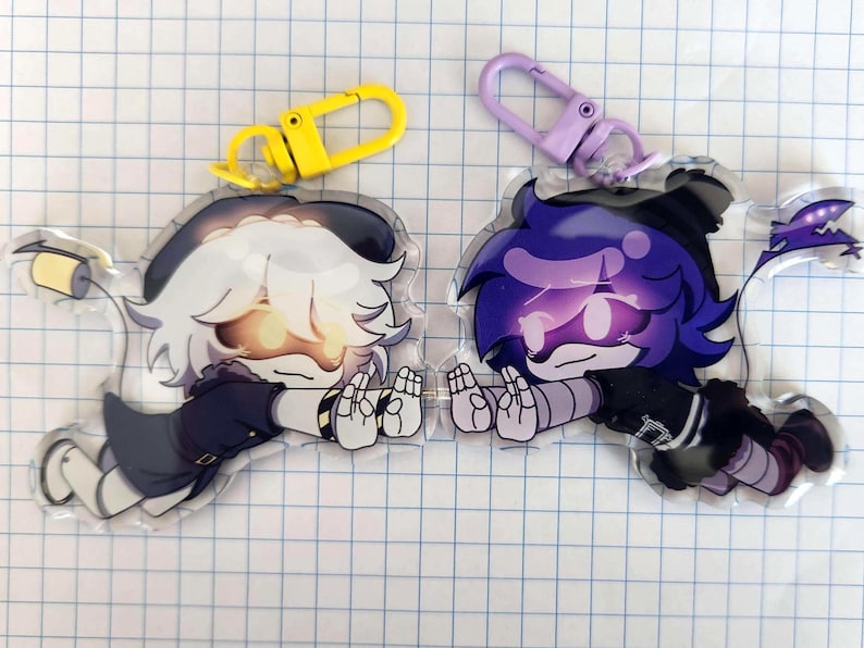 May include: Two acrylic keychains featuring anime-style characters. One has white hair and a yellow clasp, the other has purple hair and a purple clasp. Both characters are in a lying down pose with their hands up.