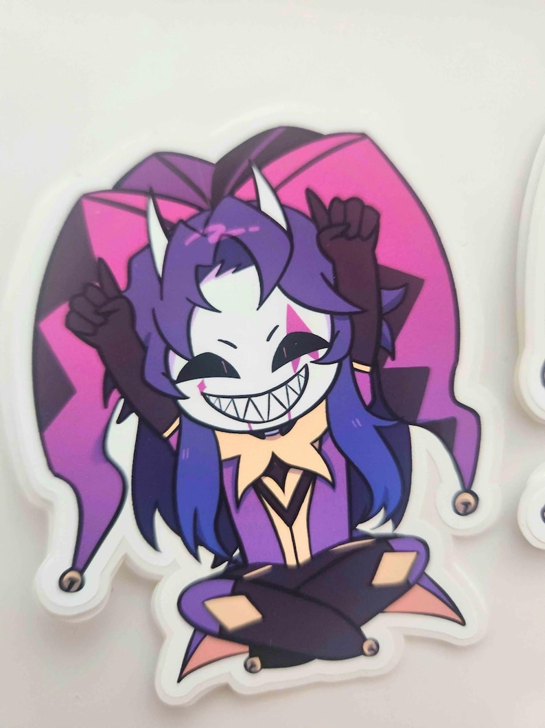 May include: A sticker featuring a cartoon jester character with a white mask, purple hair, and a purple and pink jester hat. The jester is wearing a purple outfit and has a wide, toothy grin. The sticker has a white border.
