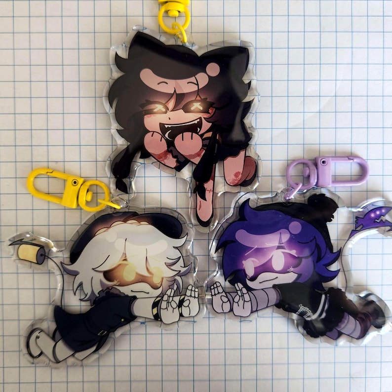 May include: Three acrylic charm keychains featuring anime-style characters with vibrant colors. The charms have yellow, and purple clasps. The characters have black, white, and purple hair, with glowing eyes and unique outfits. The charms are on a grid background.