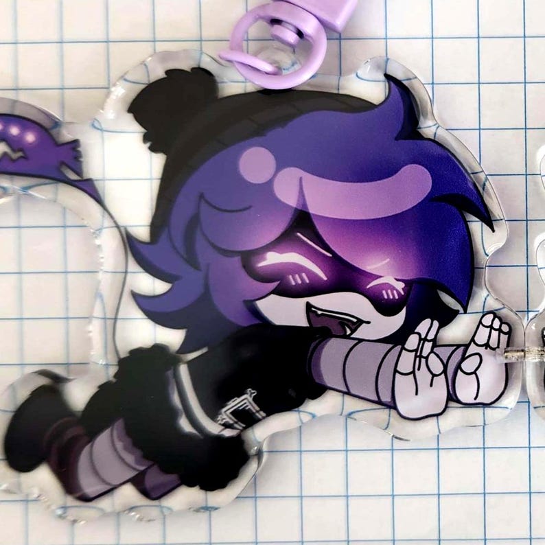 May include: A clear acrylic charm featuring a cartoon character with purple hair and glowing eyes. The character is wearing a black outfit with gray accents and is attached to a purple clasp. The charm is designed with a cartoon style.