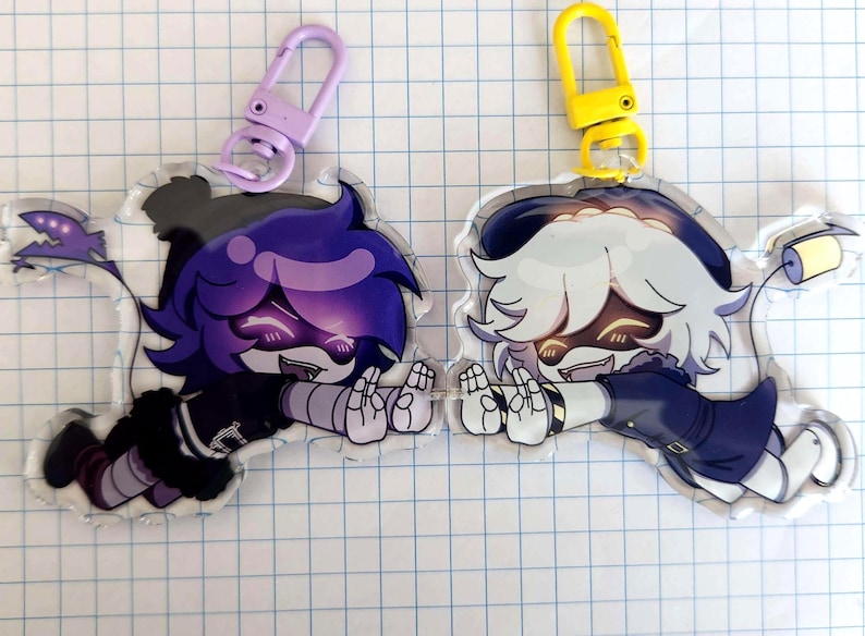 May include: Two acrylic keychains featuring cartoon characters. One has purple hair and a purple clasp, the other has white hair and a yellow clasp. Both characters are in a flying pose with a smiling expression.
