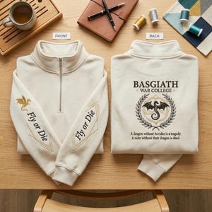 May include: Cream-colored quarter-zip sweatshirt with "Fly or Die" and a gold dragon embroidered on the sleeves. The back features a crest with a dragon and the text "BASGIATH WAR COLLEGE".