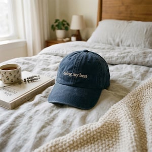 May include: A dark blue baseball cap with the text "doing my best" embroidered in white thread on the front panel. The cap features a curved brim and a structured crown, showcasing a classic six-panel design with a button on the top center.