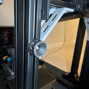 Puede incluir: Una impresora 3D negra con una pieza de plástico blanco unida al lateral. La impresora tiene una perilla negra en la parte delantera.