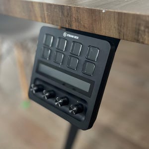 May include: A black Stream Deck with a small LCD screen and eight buttons. The device is mounted to a wooden desk.