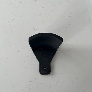Op de afbeelding: Zwarte plastic wandbeugel met twee gaten voor bevestigingsschroeven.