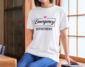May include: White t-shirt with the words "Emergency Department" in a black rectangular box, with a small pink heart above the word "Emergency". The shirt is paired with blue jeans.