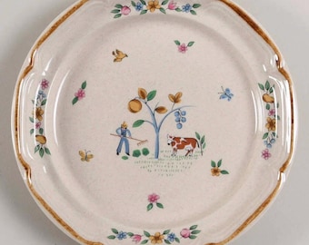 Può includere: Un piatto rotondo in ceramica con base color crema maculata e bordo smerlato marrone. Il centro presenta una scena dipinta di una persona con un rastrello accanto a un albero da frutto e una mucca marrone e bianca, circondata da piccoli fiori, uccelli e farfalle.