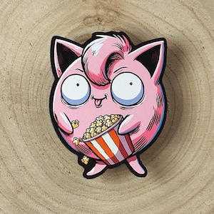 May include: A pink cartoon character with large eyes and a tongue sticking out, holding a red and white striped bucket of popcorn. The character is wearing a black and white striped shirt and has a pink and white striped tail.
