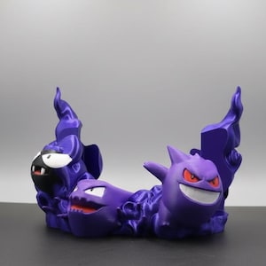 Könnte beinhalten: Eine lila 3D-gedruckte Skulptur mit drei Pokémon-Charakteren: Nebulak, Alpollo und Gengar. Die Skulptur hat ein flammenartiges Design und befindet sich vor einem neutralen Hintergrund. Die Charaktere sind in einem verspielten, cartoonartigen Stil gehalten.