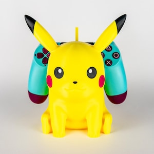 May include: A yellow Pikachu figure with black-tipped ears, red cheeks, and black eyes. A teal and maroon game controller is behind the figure. The controller has white symbols and buttons.