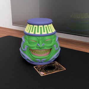 May include: A green and purple decorative container with a smiling face, a blue top, and a yellow and green design around the top. A trading card is in front of the container. The container is on a black surface.