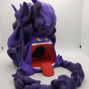 May include: A 3D-printed purple Gengar figure with a wide open mouth and a red tongue. The figure has yellow eyes and a dark purple, cloud-like base. The figure is a collectible item.