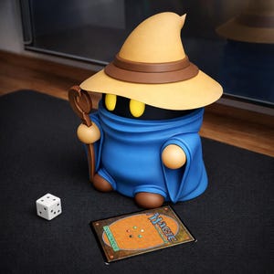 Könnte beinhalten: Eine blaue, gelbe und braune Figur eines Magiers mit Stab, Würfel und Magic: The Gathering-Karte. Der Magier hat einen großen Hut und eine blaue Robe. Der Würfel ist weiß mit schwarzen Punkten. Die Karte hat eine braune Rückseite.