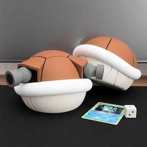 Può includere: Due figure a forma di tartaruga marrone e bianca con cannoni grigi, che assomigliano a un personaggio popolare. Sono presenti anche una carta collezionabile e un dado bianco con due punti. Le figure sono su una superficie nera.