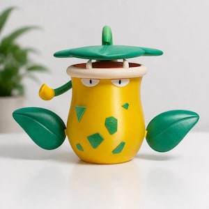 Puede incluir: Un personaje amarillo estilizado con elementos y acentos verdes en forma de hojas. El personaje tiene un cuerpo redondo con formas geométricas verdes, un sombrero verde y dos hojas verdes a los lados. Tiene una boca blanca y ojos enojados.