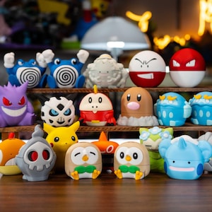 May include: A collection of colorful Pokémon character figures, including Pikachu, Gengar, and others, arranged on wooden shelves and a tabletop. The figures are various shapes and sizes, with bright colors and detailed designs. The background is blurred, with a warm, inviting glow.