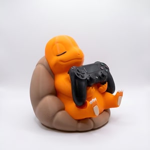 Könnte beinhalten: Eine leuchtend orangefarbene Kreaturenfigur mit geschlossenen Augen, die in einem braunen Sitzsack sitzt und einen schwarzen Videospiel-Controller hält. Die Figur hat eine glatte Oberfläche, helle Krallen an den Füßen und eine entspannte Haltung.